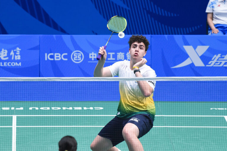 Atleta de Badminton de frente, com raquete erguida para acertar a peteca