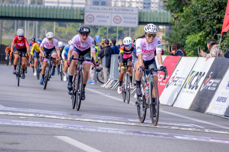 Ciclistas femininas cruzam a linha de chegada da prova de resistência com Talita na liderança