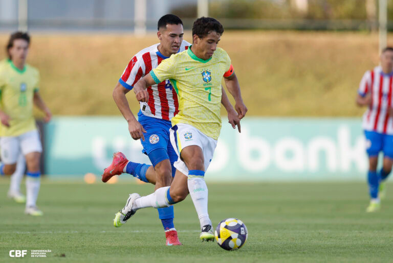 Jogador do Brasil avança com a bola dominada sendo perseguido por paraguaio.