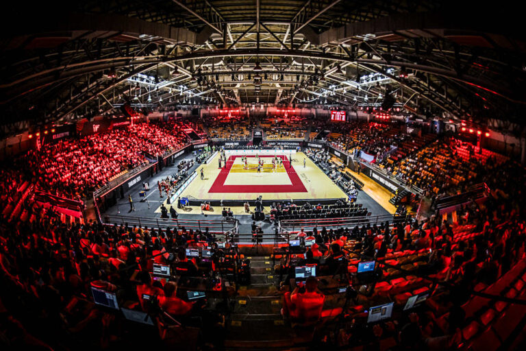 Foto do ginásio com luzes vermelhas e quadra cor creme.