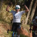 João Pedro Rossi ergue os braços sobre a bicicleta para comemorar a vitória.