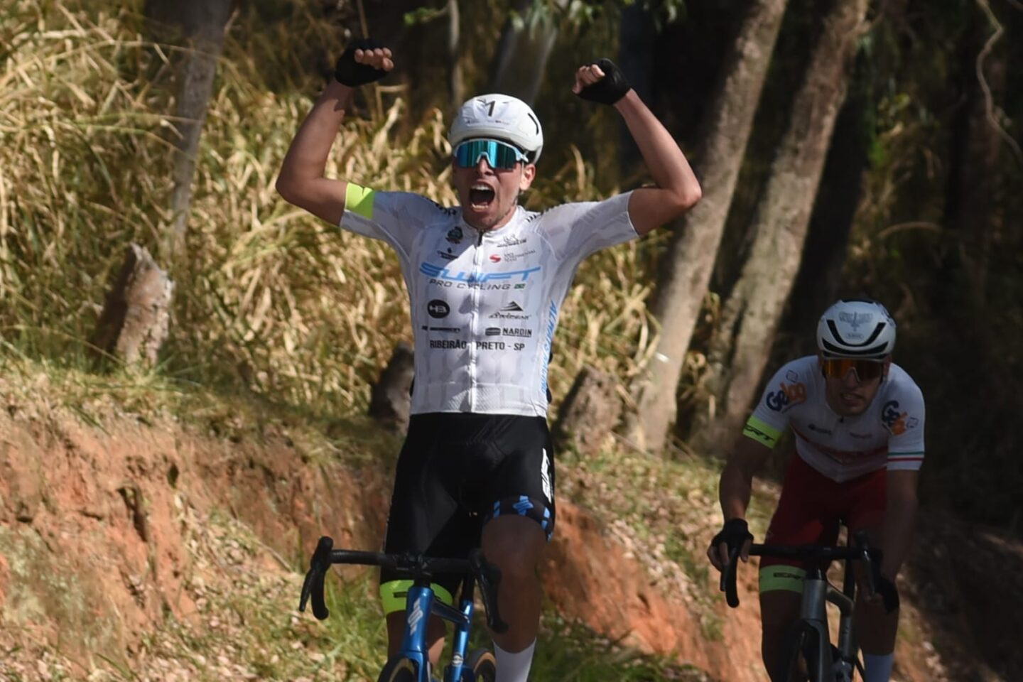 João Pedro Rossi ergue os braços sobre a bicicleta para comemorar a vitória.