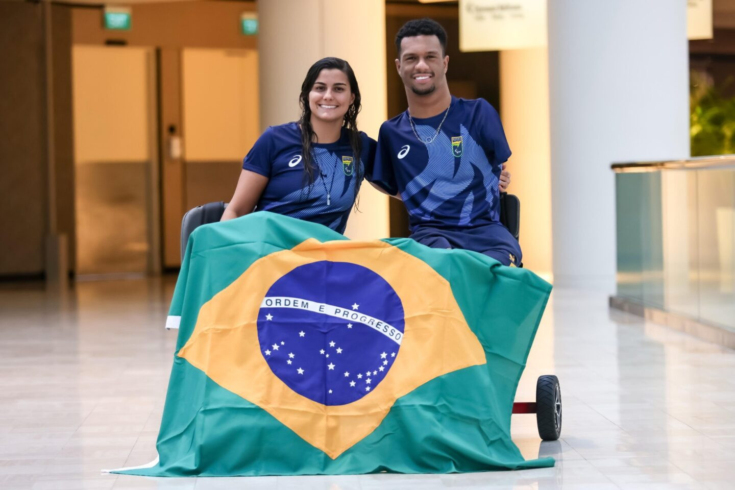 Mariana Gesteira e Gabriel Araújo com bandeira do Brasil ao fundo